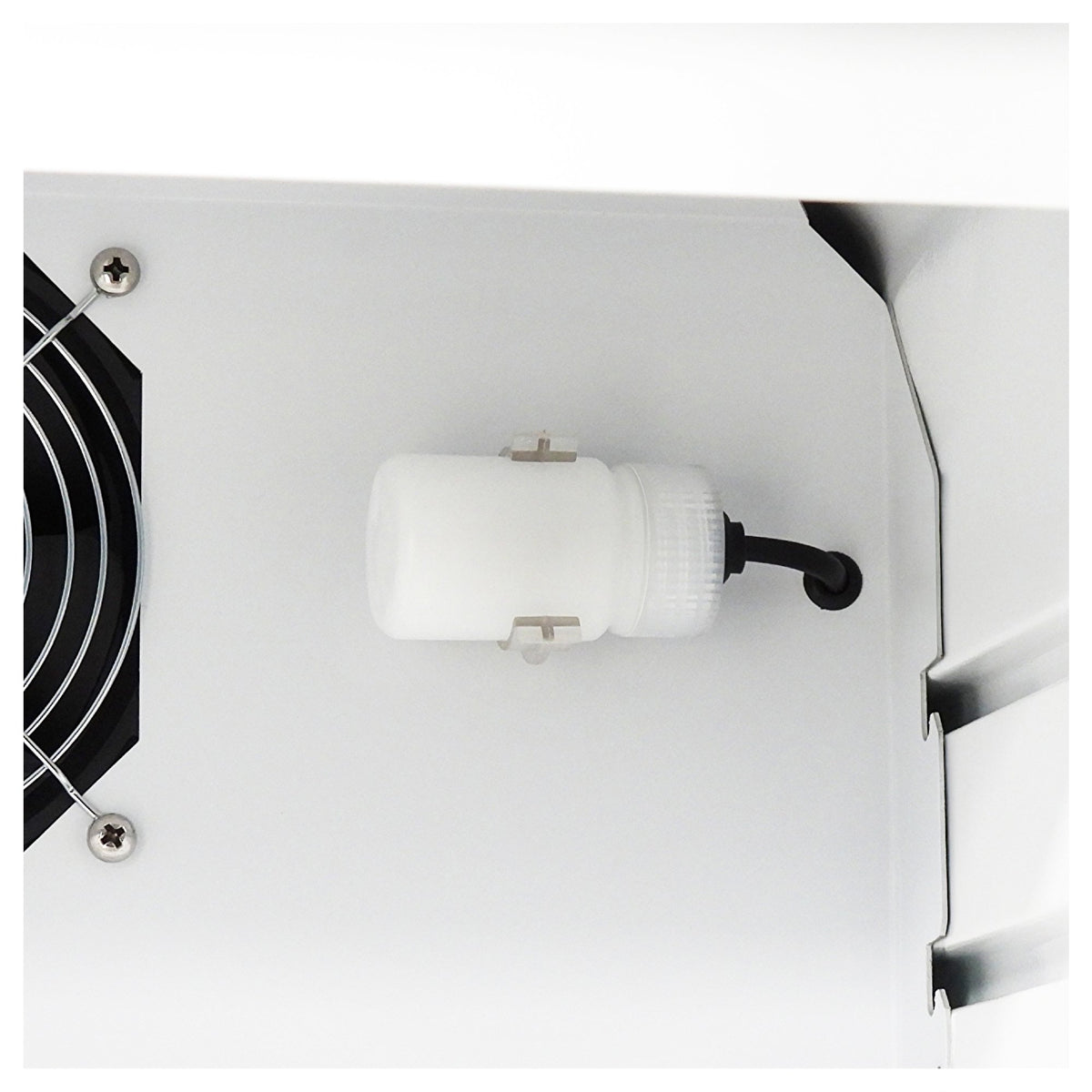 Close-up of a white cylindrical component with a black cable attached, mounted on a white metal surface next to a black fan grille.